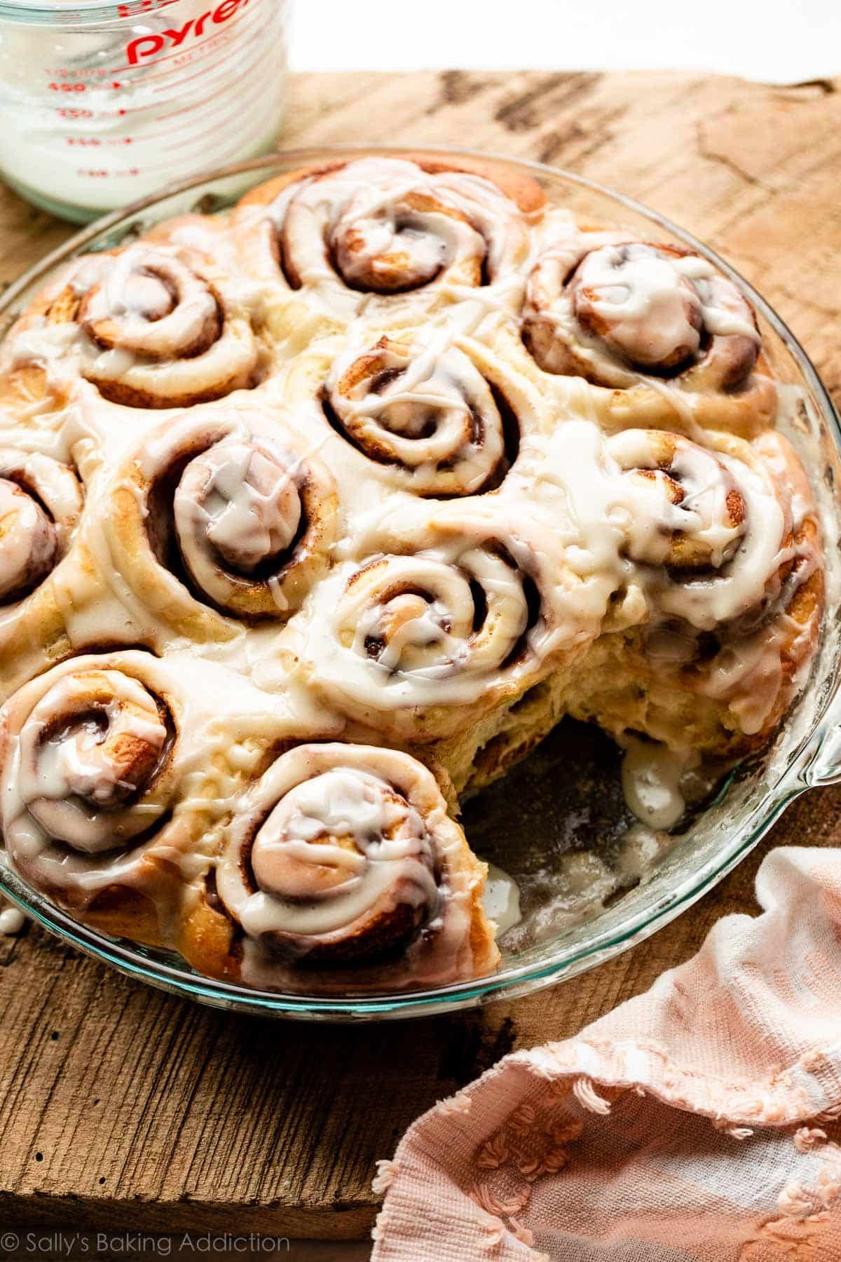 glass dish of cinnamon rolls topped with coffee vanilla icing and 1 cinnamon roll removed.
