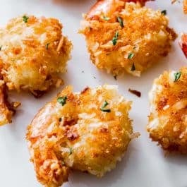 close-up of 6 coconut shrimp on white cutting board.
