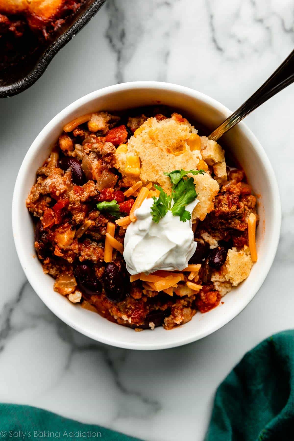 cornbread and chili in white bowl with sour cream and cheese on top.