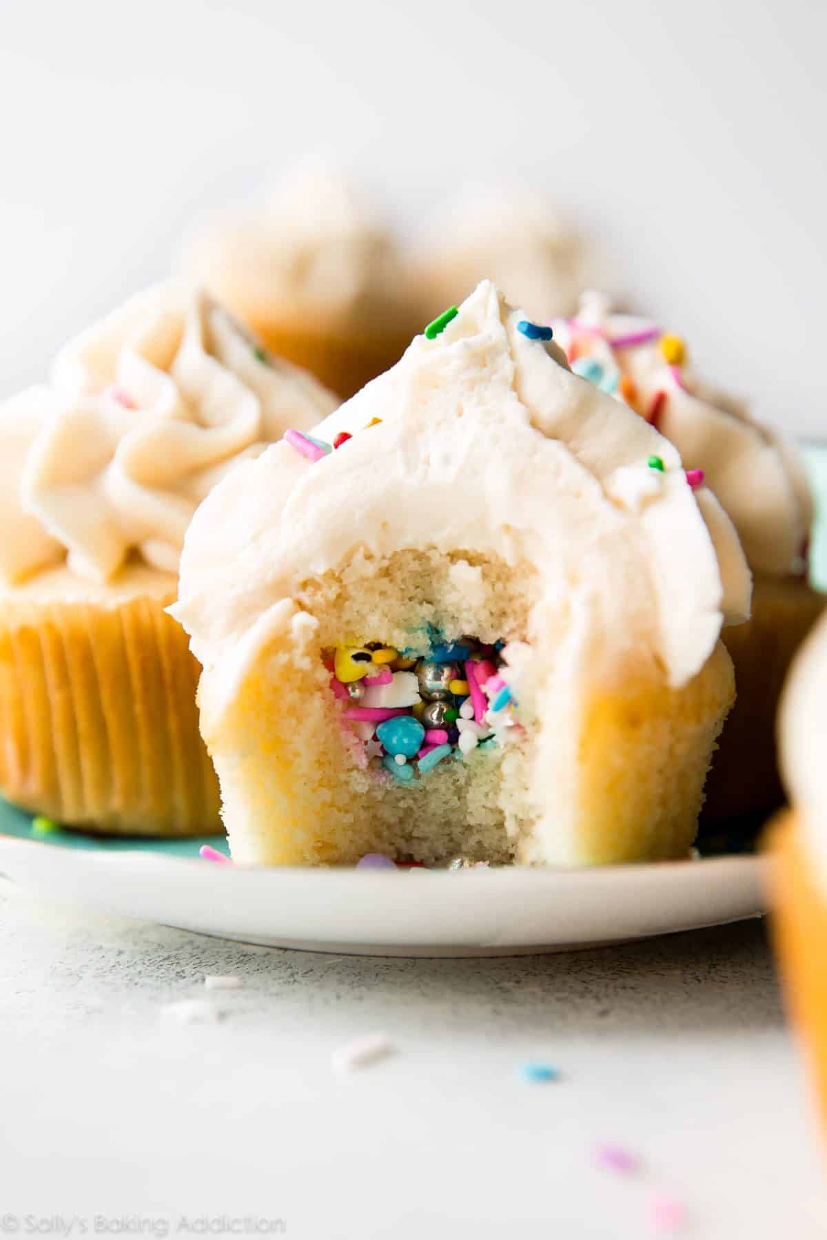 piñata cupcakes on a plate with a bite taken from one showing the sprinkles in the middle