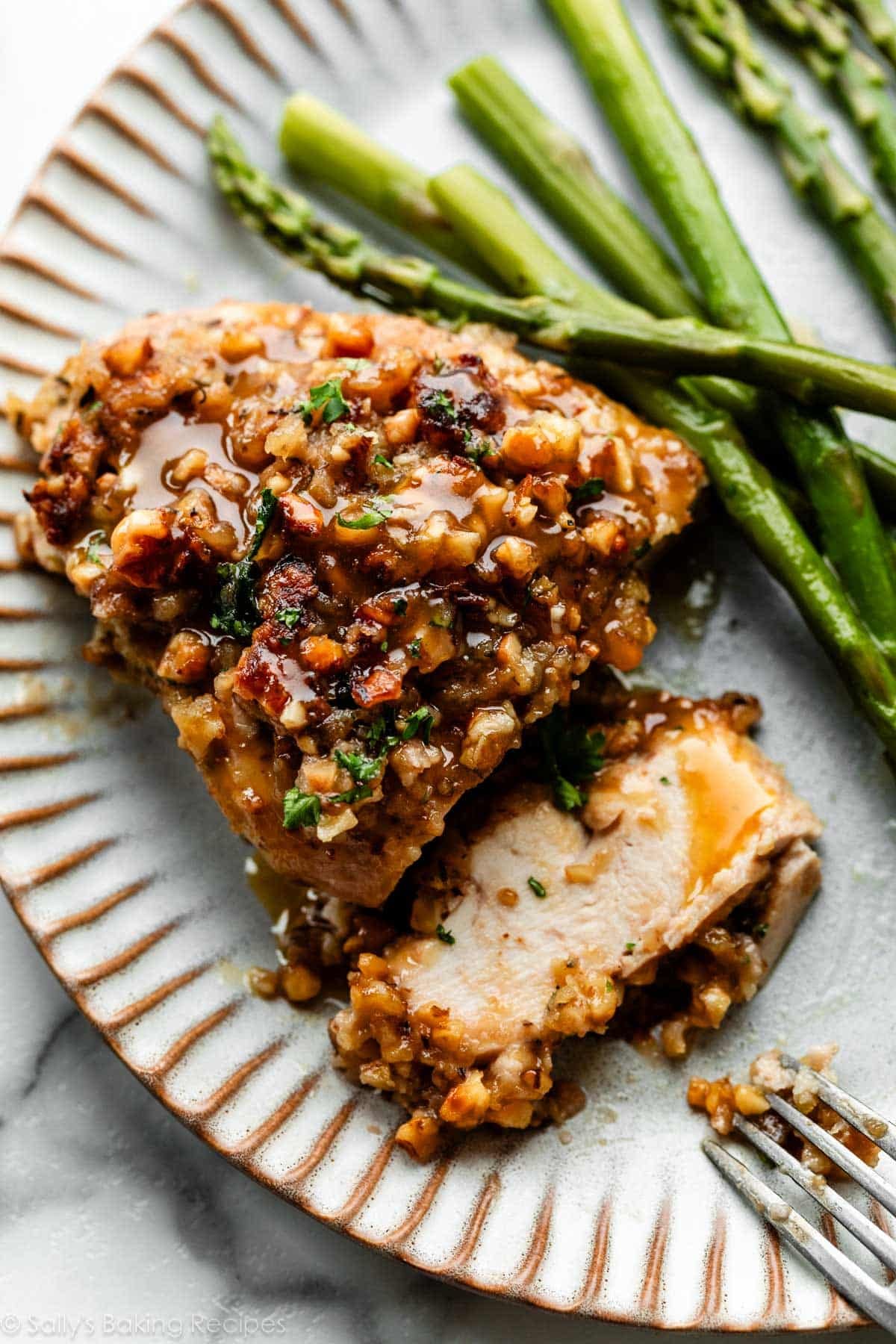 sliced walnut chicken with honey mustard glaze on gray plate with asparagus.