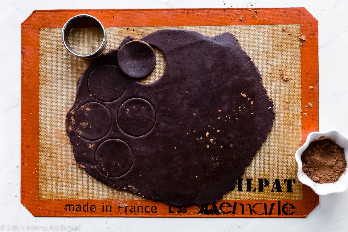 Chocolate sugar cookie dough rolled out onto silpat baking mat with a round cookie cutter