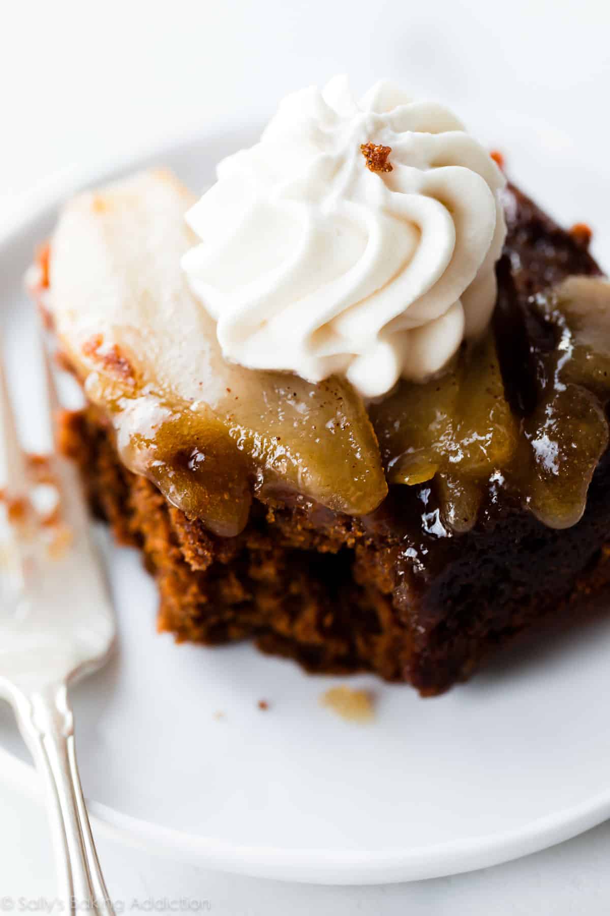 slice of upside down pear gingerbread with whipped cream on a white plate