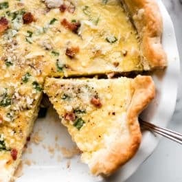 Quiche with bacon in a white pie dish with a slice being removed