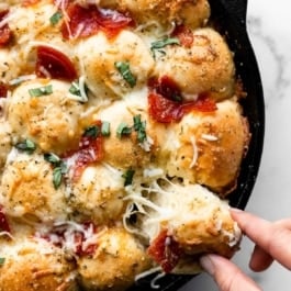 pulling a cheese pepperoni pizza roll out of cast iron skillet.