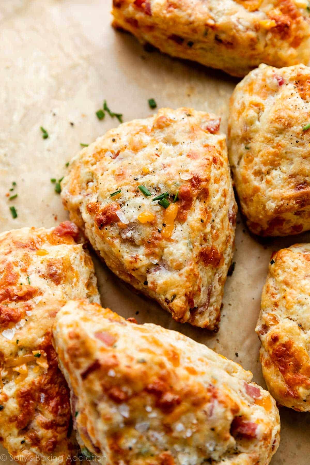 ham and cheddar cheese scones with chives and sea salt garnish on top sitting on brown parchment paper.