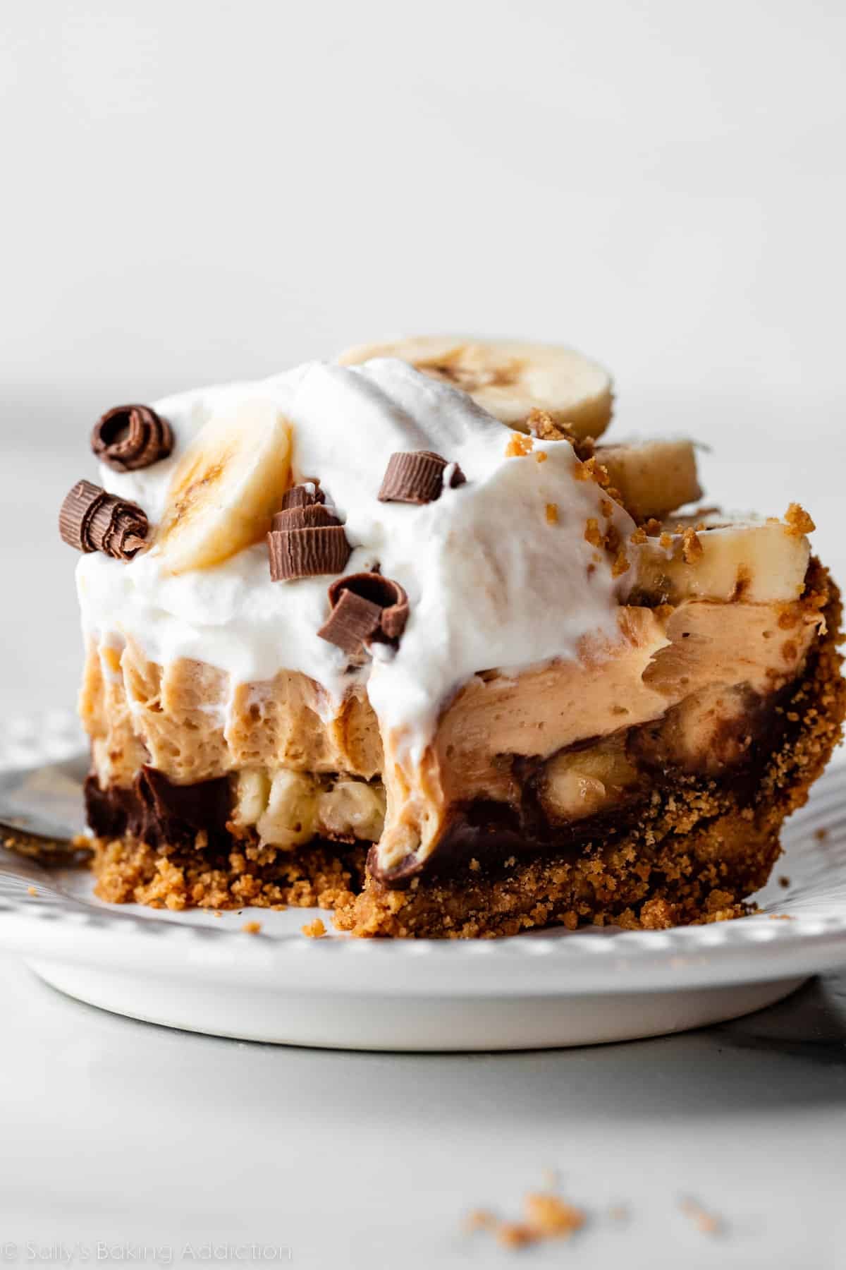 slice of peanut butter and banana cream pie with forkful taken out on white plate.