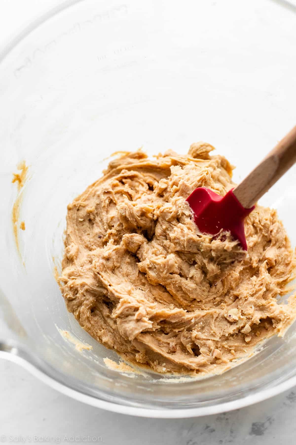 bowl of cookie dough with red spatula in it.