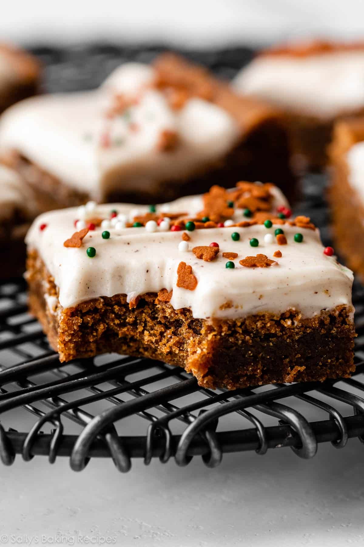 frosted gingerbread cookie bar with bite taken out on black wire cooling rack.