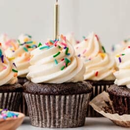 chocolate cupcakes with vanilla buttercream, rainbow sprinkles, and a gold birthday candle.
