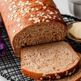 whole wheat bread loaf with two slices cut on black wire rack.