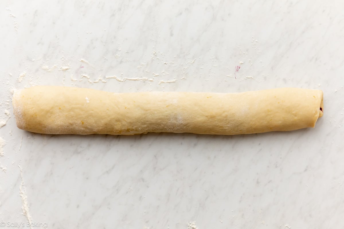 dough rolled up into a log on a marble surface.